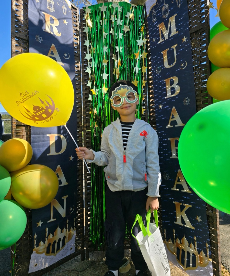 A child celebrating Eid with balloons in front of Ramadan Mubarak banners